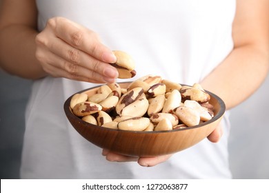 Woman Holding Bowl With Brazil Nuts On Grey Background, Closeup