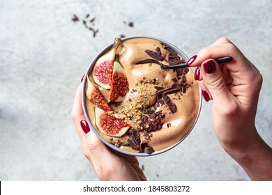 Woman Holding Bowl Of Chocolate Smoothie With Figs And Hemp Seeds, Gray Background. Healthy Vegan Food Concept.