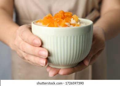 Woman Holding Bowl Of Delicious Rice Pudding With Dried Apricots, Closeup