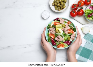 Woman holding bowl of delicious salad with canned tuna at white table, top view. Space for text
