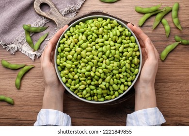 Woman Holding Bowl Of Edamame Beans At Wooden Table, Top View