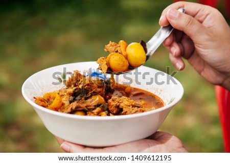 Woman holding bowl of local exotic chicken immature egg hot curry - Thai cluster of egg spicy curry on spoon. close up shot