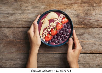 Woman Holding Bowl Of Tasty Acai Smoothie On Wooden Table