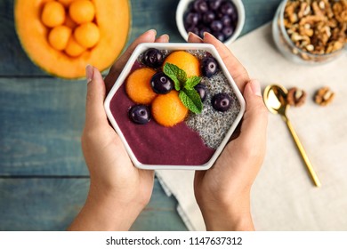 Woman Holding Bowl Of Tasty Acai Smoothie Over Wooden Table