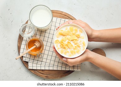 Woman holding bowl with tasty cornflakes on light background
