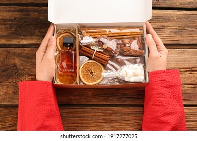 Woman holding box with stylish craft gift set at wooden table, top view