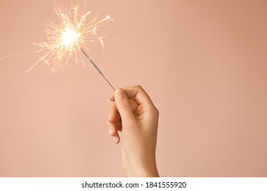 Woman holding bright burning sparkler on beige background, closeup - Powered by Shutterstock