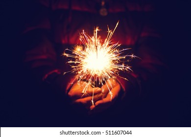 Woman holding bright festive Christmas sparkler in hand, tinted photo
