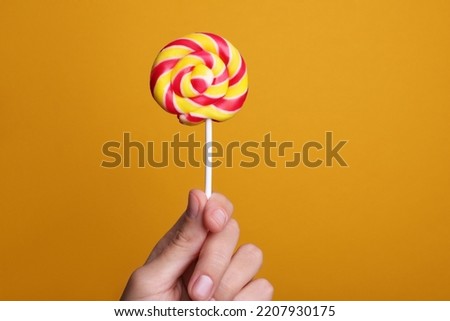 Woman holding bright tasty lollipop on orange background, closeup