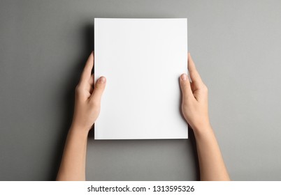 Woman holding brochure with blank cover on grey background, top view. Mock up for design