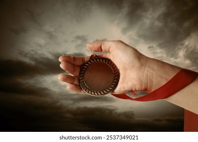 Woman holding bronze medal in hand against sunset sky, closeup - Powered by Shutterstock