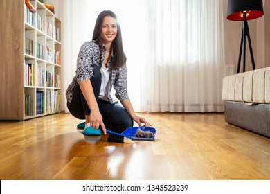 Woman Holding A Broom And Sweeping Floor, Collecting Dust Onto A Dustpan