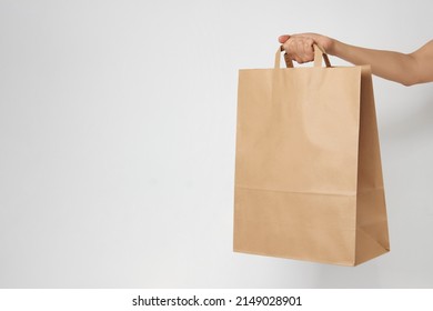 Woman Holding Brown Paper Bag On White Background With Copy Space. Delivery And Shipping Service Concept. Hand With Paper Shopping Bag, Close-up.