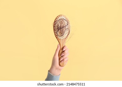 Woman holding brush with fallen down brunette hair on yellow background