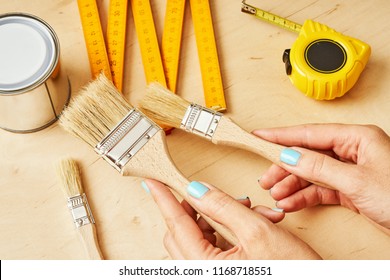 woman holding brushes to paint in her hands over a wooden table with tools