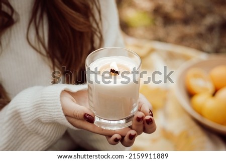 Woman holding burning candle in hands outdoors. Having picnic, relax outdoors in autumn park