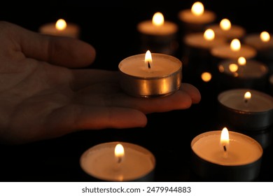 Woman holding burning tealight candle on black background, closeup - Powered by Shutterstock