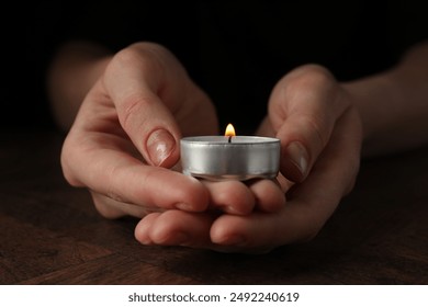 Woman holding burning tealight candle at wooden table, closeup - Powered by Shutterstock