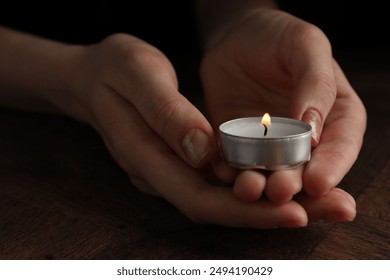 Woman holding burning tealight candle at wooden table, closeup - Powered by Shutterstock