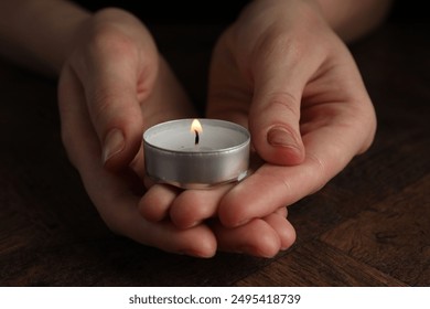 Woman holding burning tealight candle at wooden table, closeup - Powered by Shutterstock