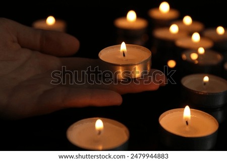 Woman holding burning tealight candle on black background, closeup
