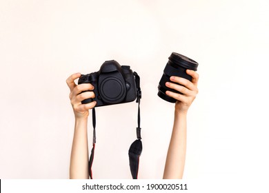 Woman holding a camera body and a lens on white wall background.