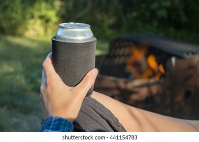 Woman Holding A Can Of Beer In A Sleeve By The Fire While Camping