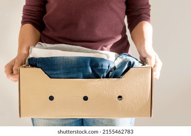 Woman holding cardbox with women's casual all-season clothes.  Storage concept . Reuse, recycle, charity concept. Make donation to poor needy people - Shutterstock ID 2155462783