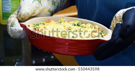 Woman holding casserole dish of Mexican cheese dip with oven mitts
