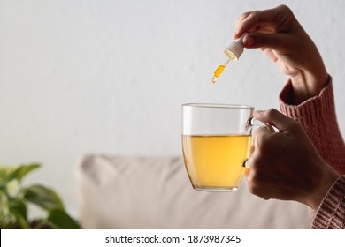 Woman holding Cbd hemp oil Cannabis in tea cup at home - Alternative medicine concept - Focus on hand
