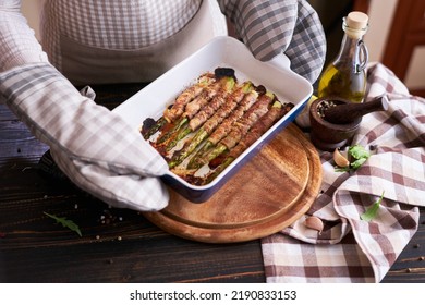 Woman Holding Ceramic Baking Dish With Baked Aspargus Covered With Bacon