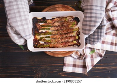 Woman Holding Ceramic Baking Dish With Baked Aspargus Covered With Bacon