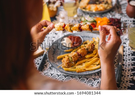 woman holding chicken pieces on skewers sprinkled with sesame