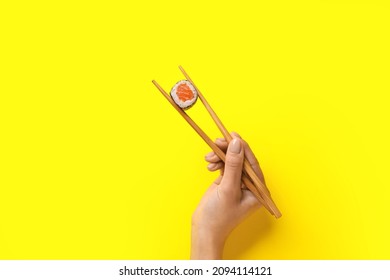 Woman holding chopsticks with delicious maki roll on color background