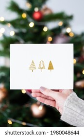 Woman holding a Christmas card in front of a Christmas tree mockup