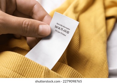 Woman holding clothing label on yellow garment, closeup - Powered by Shutterstock