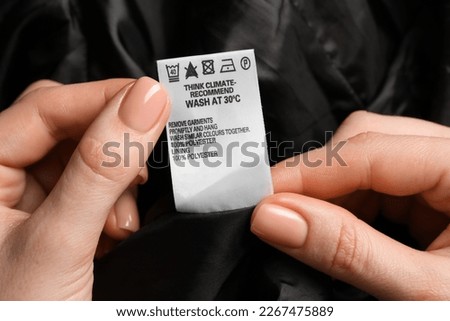 Woman holding clothing label on black garment, closeup