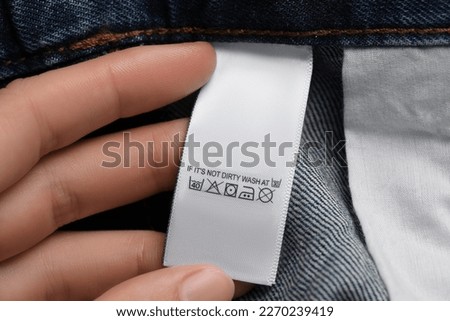 Woman holding clothing label on jeans garment, closeup