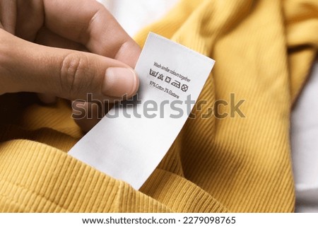 Woman holding clothing label on yellow garment, closeup