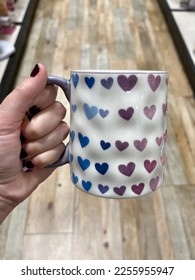 A woman holding coffee mug that has gradient colorful hearts it  They are pink  purple    blue 