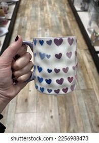 A woman holding coffee mug that has gradient colorful hearts it  They are pink  purple    blue 