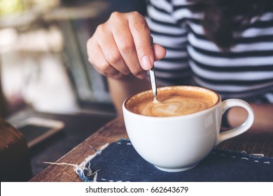 A woman holding coffee spoon and stirring hot coffee on wooden table