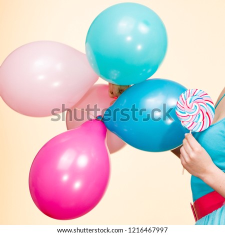 Woman holding colorful balloons and sweet lollipop in hands. Summer holidays, celebration and happiness concept. Studio shot bright yellow