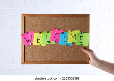 Woman Holding Corkboard With Word Welcome Near White Brick Wall, Closeup