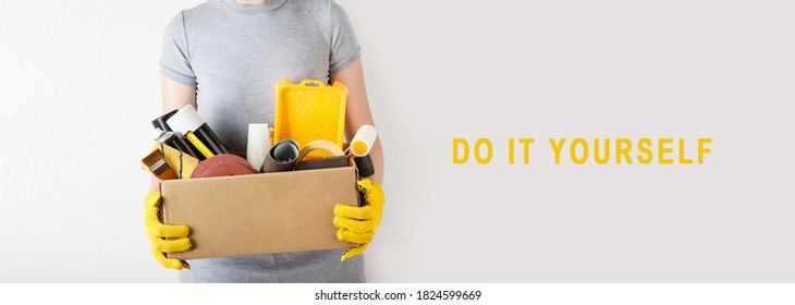 Woman holding craft box with repair tools. Cardboard box filled with paints, brushes, roller, sandpaper, measuring tape, wallpaper in woman's hands. Concept of renovation banner. DIY repair in a room