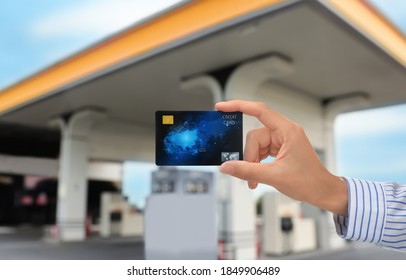 Woman holding credit card against blurred gas station, closeup. Cashless payment