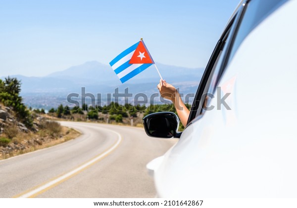 Woman holding\
Cuba flag from the open car window driving along the serpentine\
road in the mountains.\
Concept