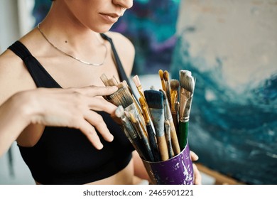 A woman holding a cup full of paintbrushes, ready to create something beautiful. - Powered by Shutterstock