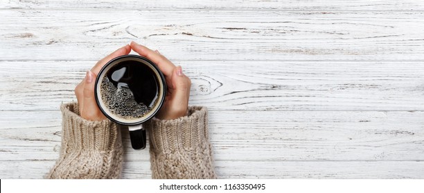 Woman Holding Cup Of Hot Coffee On Rustic Wooden Table, Closeup Photo Of Hands In Warm Sweater With Mug, Winter Morning Concept, Top View. Banner.