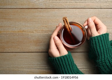 Woman Holding Cup Of Hot Tea With Aromatic Cinnamon At Wooden Table, Top View. Space For Text